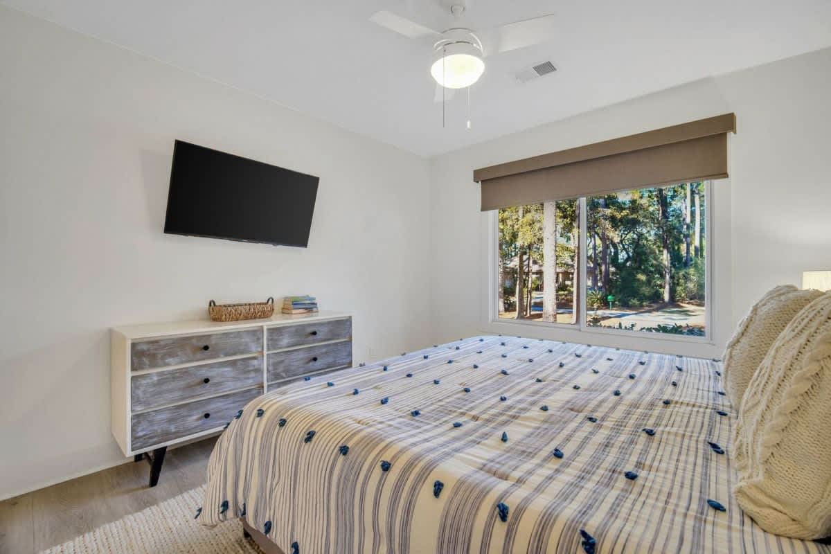 Relax in your peaceful bedroom with garden views, wall-mounted TV, and fresh coastal breezes from the ceiling fan.