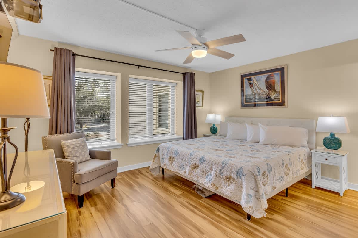 Unwind in your serene bedroom featuring polished hardwood floors, a comfortable reading chair, and gentle natural light filtering through the windows.