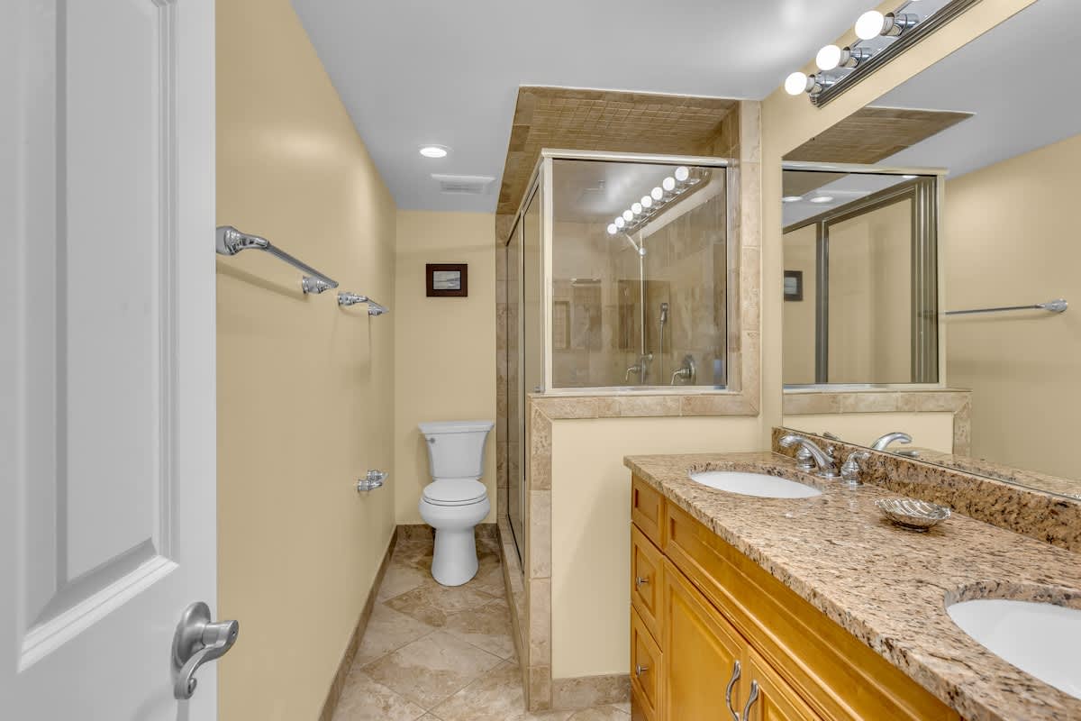 Unwind in this elegant bathroom featuring granite countertops, dual vanities, and a spacious glass-enclosed shower for your comfort.