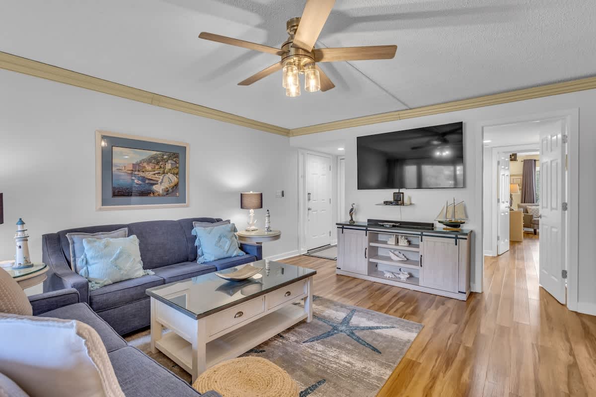 Relax in your coastal-inspired living room with plush seating, elegant ceiling fan, and entertainment center—perfect for unwinding after beach days.