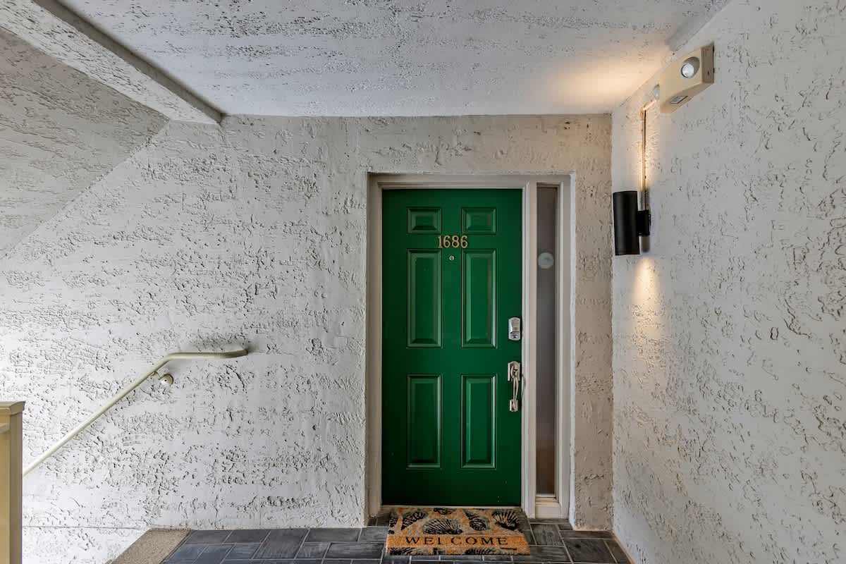A welcoming green door marked 1686 greets you at this charming entrance, complete with warm lighting and a friendly welcome mat.