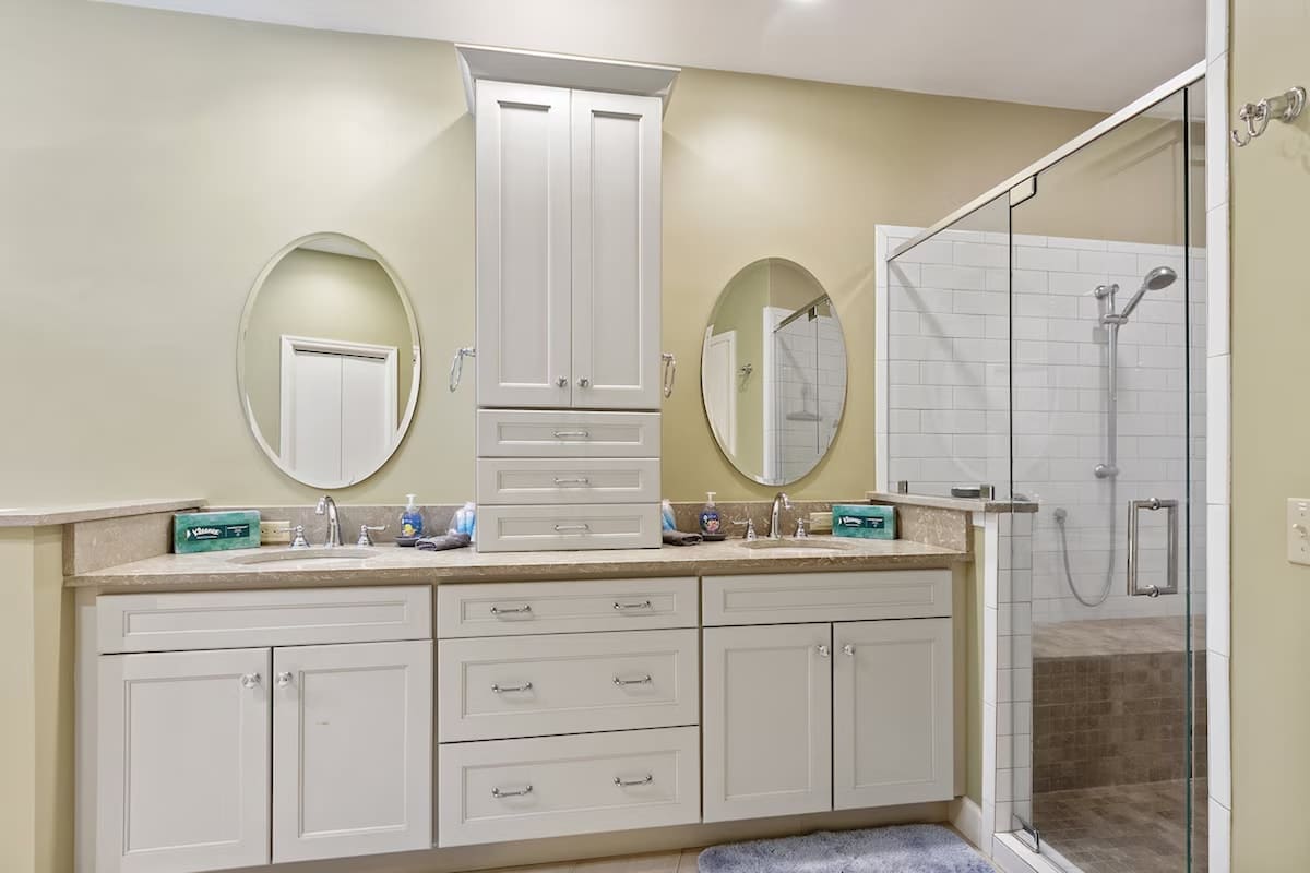 Your spacious bathroom features dual vanities with elegant mirrors and a luxurious glass-enclosed shower with subway tiles.