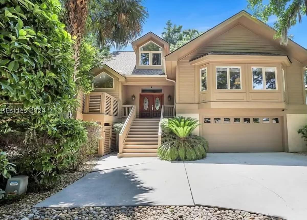 A welcoming coastal home featuring warm wood exterior, red front doors, and tropical landscaping with convenient parking.