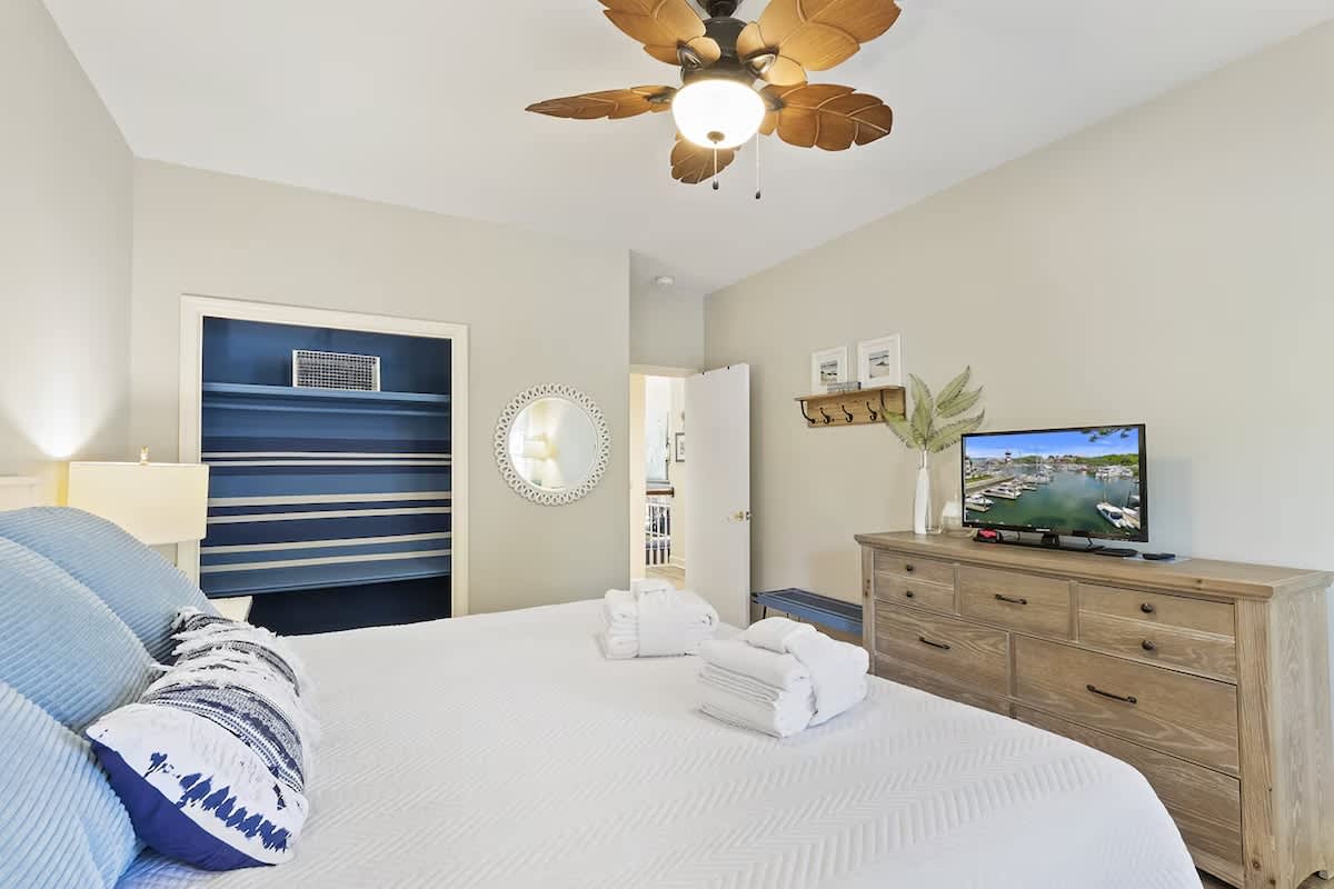 Unwind in your peaceful bedroom with coastal charm, featuring a plush bed, tropical ceiling fan, and entertainment center for perfect relaxation.