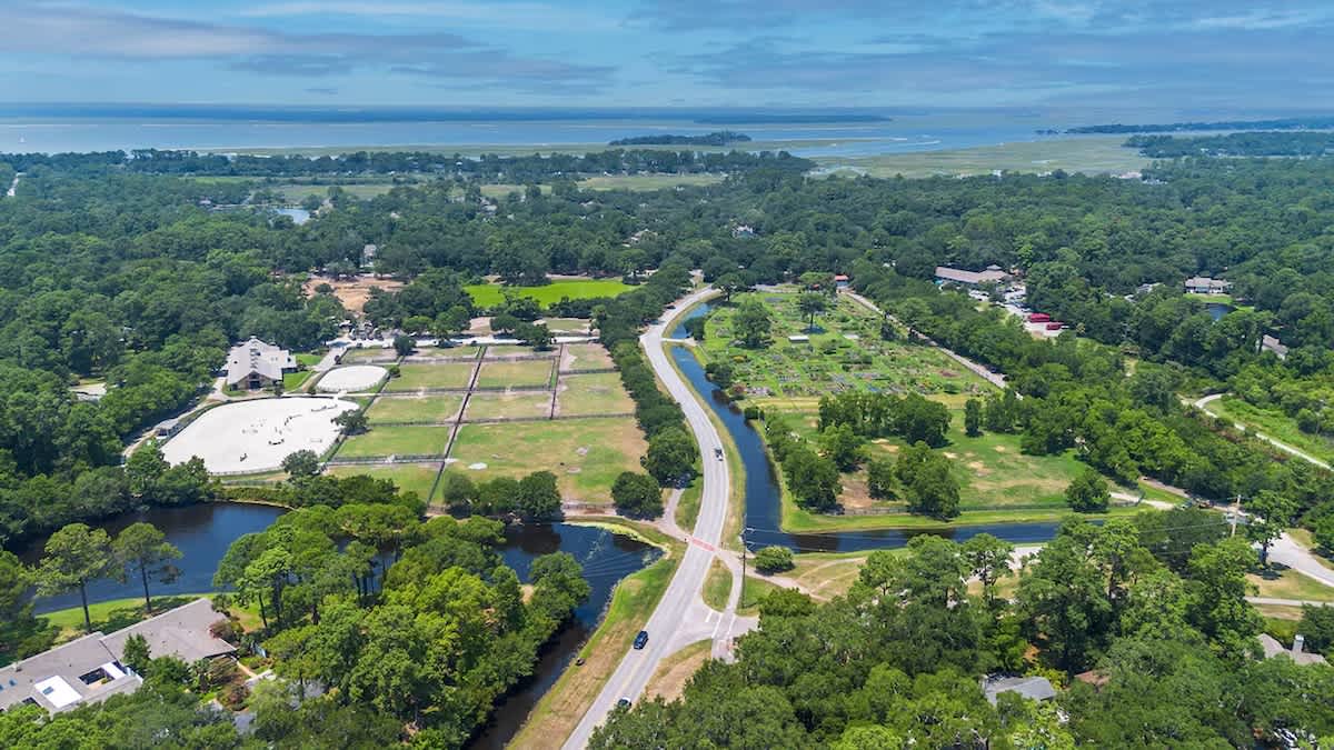 Aerial view showcasing the property's scenic coastal location, surrounded by lush forests and winding waterways leading toward the distant shoreline.