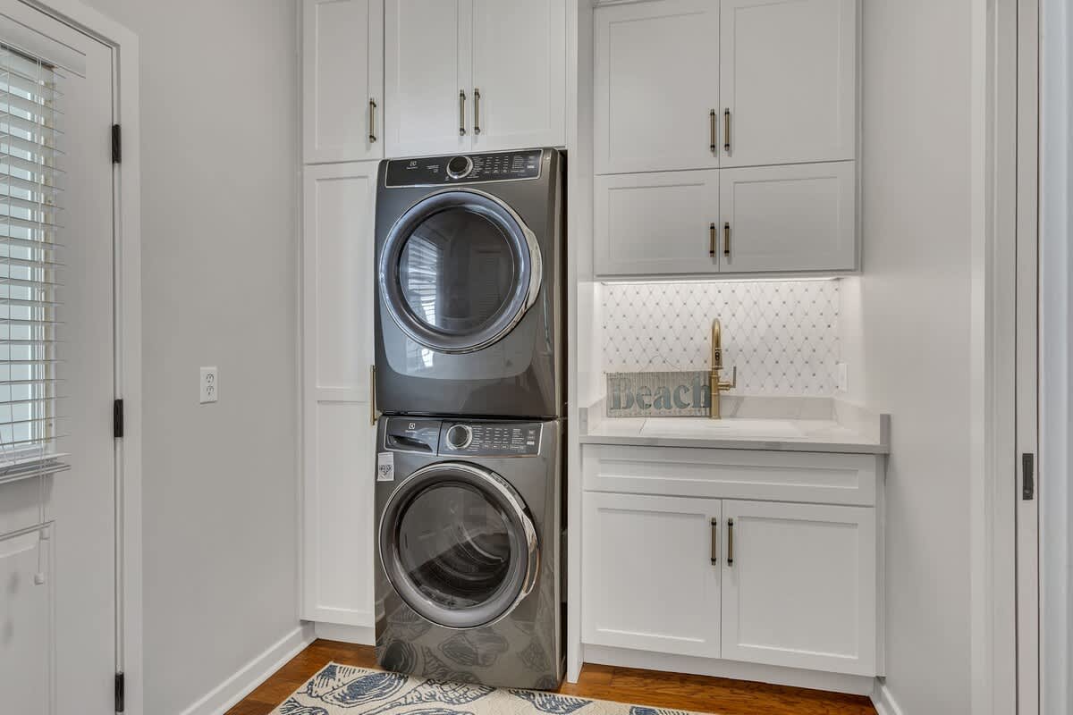 Your private laundry room features stacked washer and dryer, elegant white cabinetry, and a convenient utility sink for effortless care.