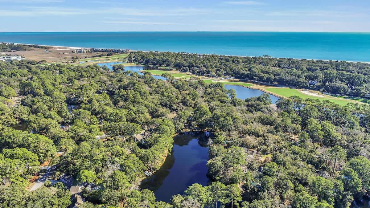 Stunning aerial view showcases the coastal property's prime location, nestled between pristine beaches and championship golf course fairways with scenic water features.