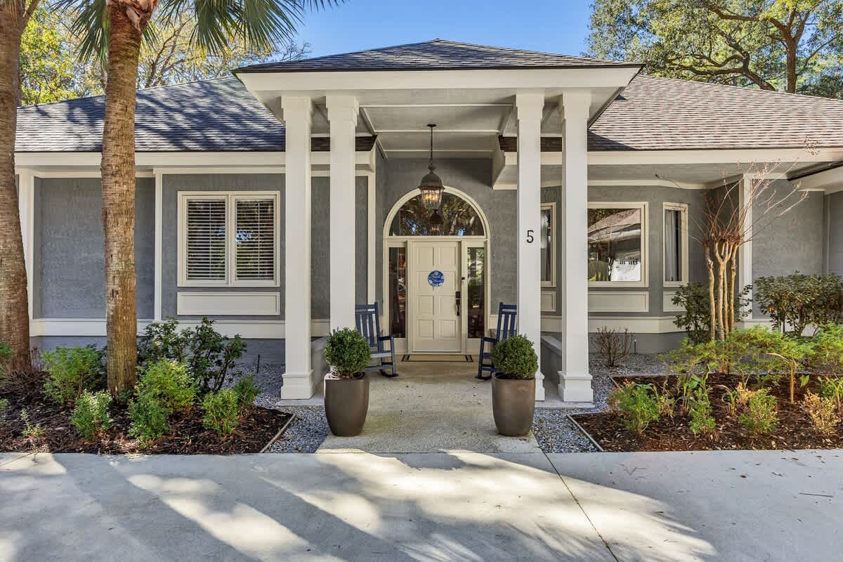 Charming property entrance with covered porch, tropical landscaping, and welcoming front door surrounded by mature palm trees and lush greenery.