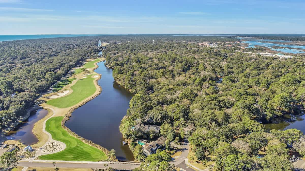 Stunning aerial view showcasing a championship golf course winding along pristine waterways, surrounded by lush coastal forest and nearby ocean views.