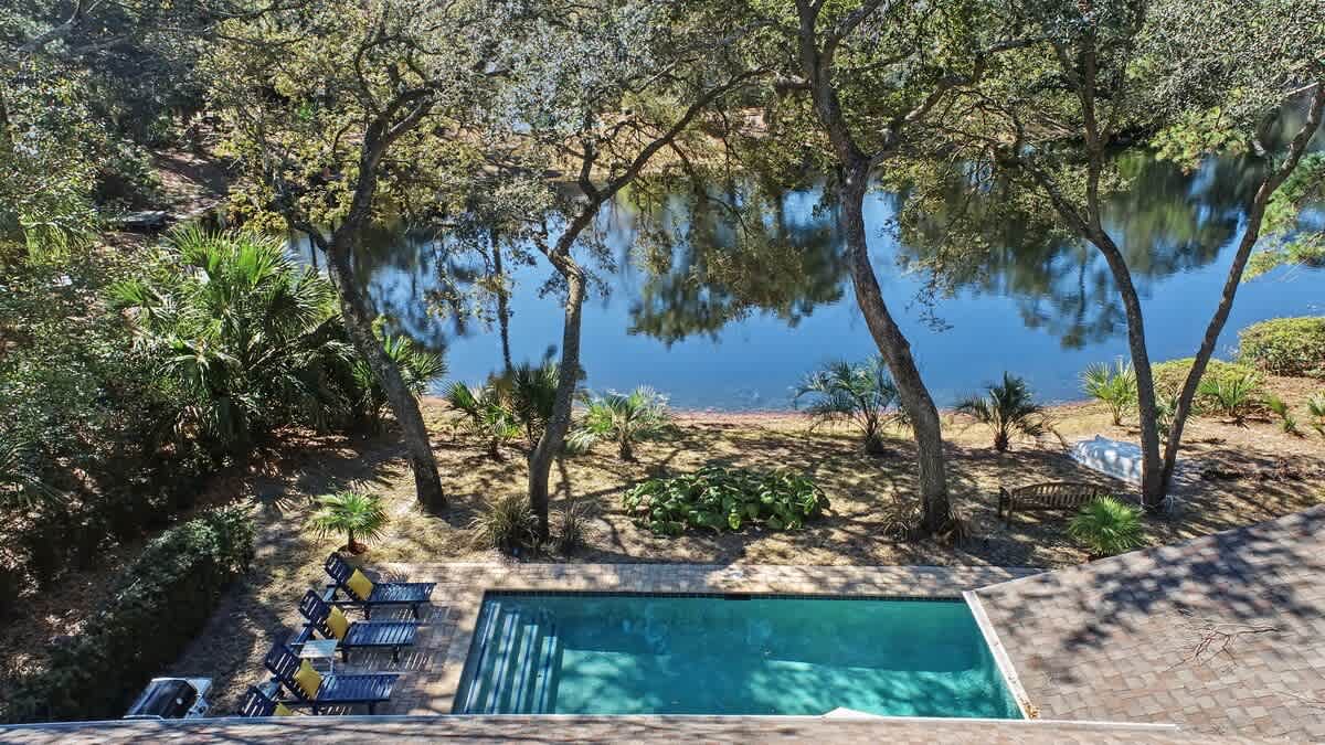 Aerial view of the property's sparkling pool area surrounded by mature trees and landscaped gardens, with waterfront access nearby.