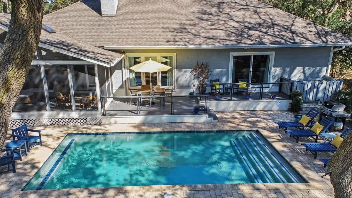 Beautiful vacation home featuring a private swimming pool, spacious deck with outdoor dining, and screened porch surrounded by mature trees.