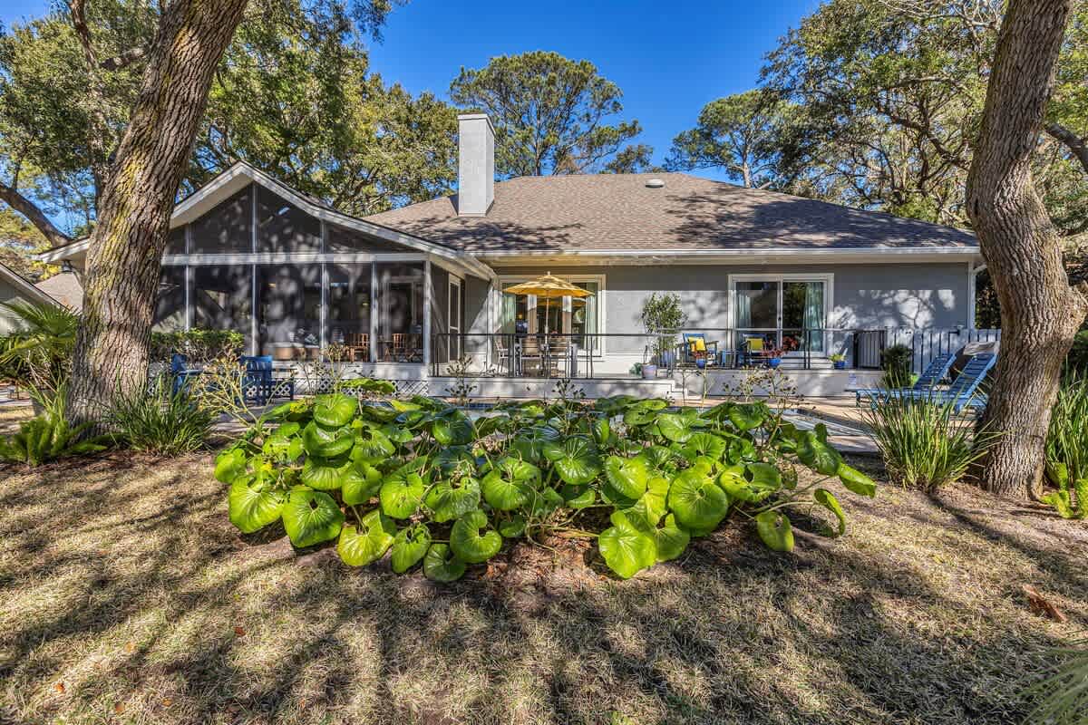 Charming single-story home nestled among mature trees with lush gardens and screened porch areas for outdoor relaxation.