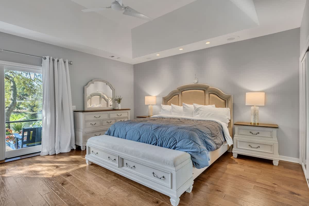 Relax in your peaceful bedroom sanctuary with elegant coastal furnishings, soft linens, and garden views from your private balcony.