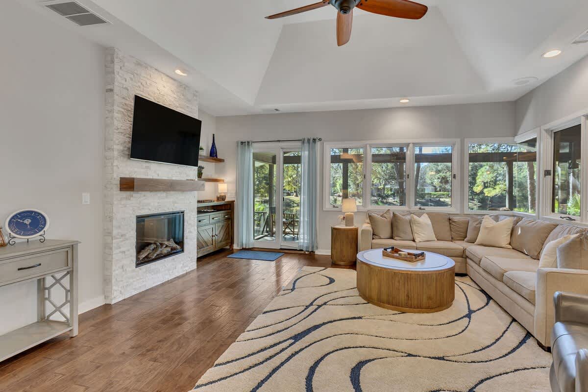 Relax in your spacious living room with cozy sectional seating, crackling fireplace, and peaceful garden views through expansive windows.