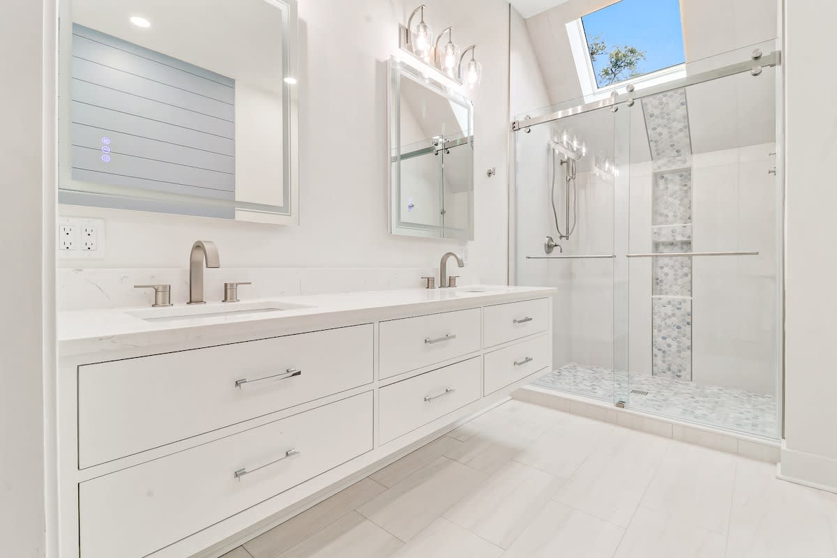 Indulge in luxury with this pristine bathroom featuring dual vanities, spa-like walk-in shower, and skylight bringing natural light.