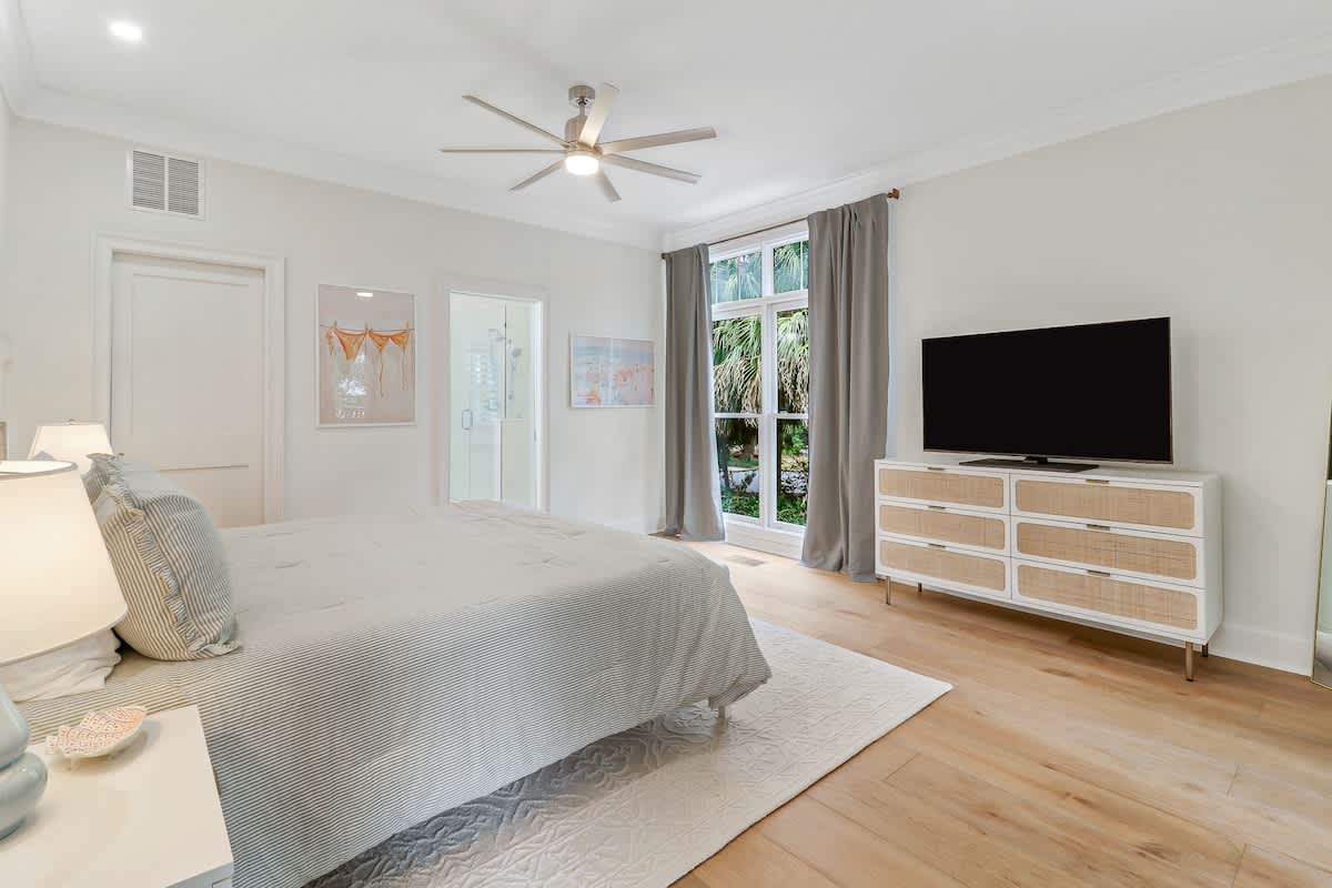 Unwind in your serene master bedroom with ceiling fan comfort, garden views through French doors, and modern entertainment center for perfect relaxation.