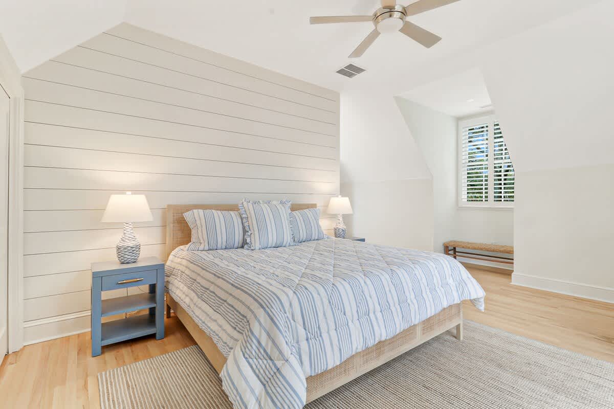 Drift off to sleep in your bright, coastal-inspired bedroom with soft striped linens and warm natural light filtering through shuttered windows.