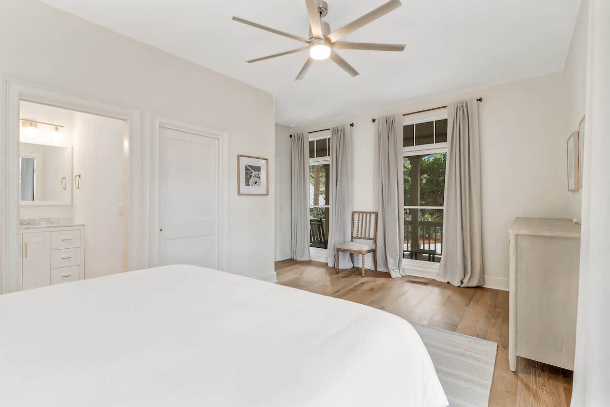 Drift off in your serene bedroom featuring crisp white linens, warm hardwood floors, and gentle natural light streaming through French doors to your private balcony.