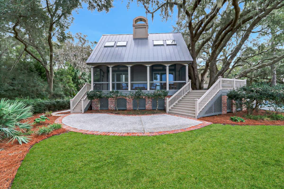 Charming cottage nestled among towering oaks with welcoming front porch and beautifully landscaped grounds surrounded by lush natural beauty.