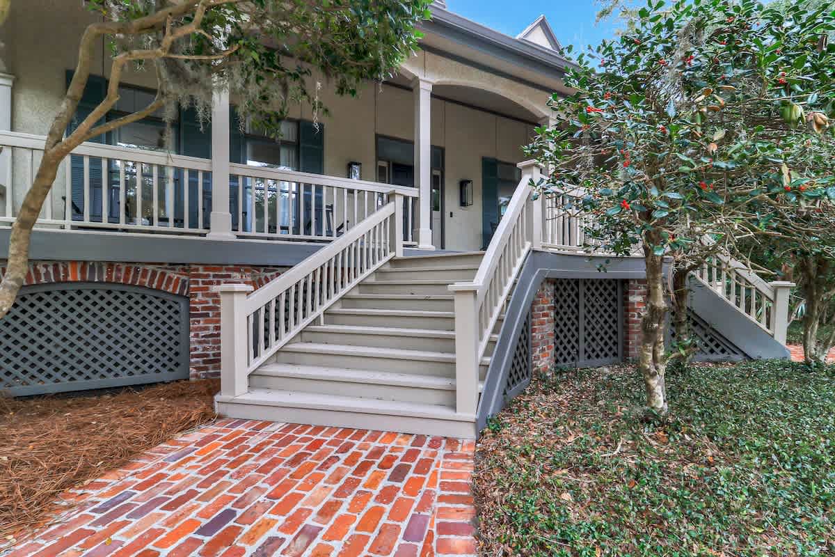 A charming Lowcountry exterior with a grand front porch, brick steps, and a sweeping driveway, all nestled beneath mature trees for a serene island welcome.
