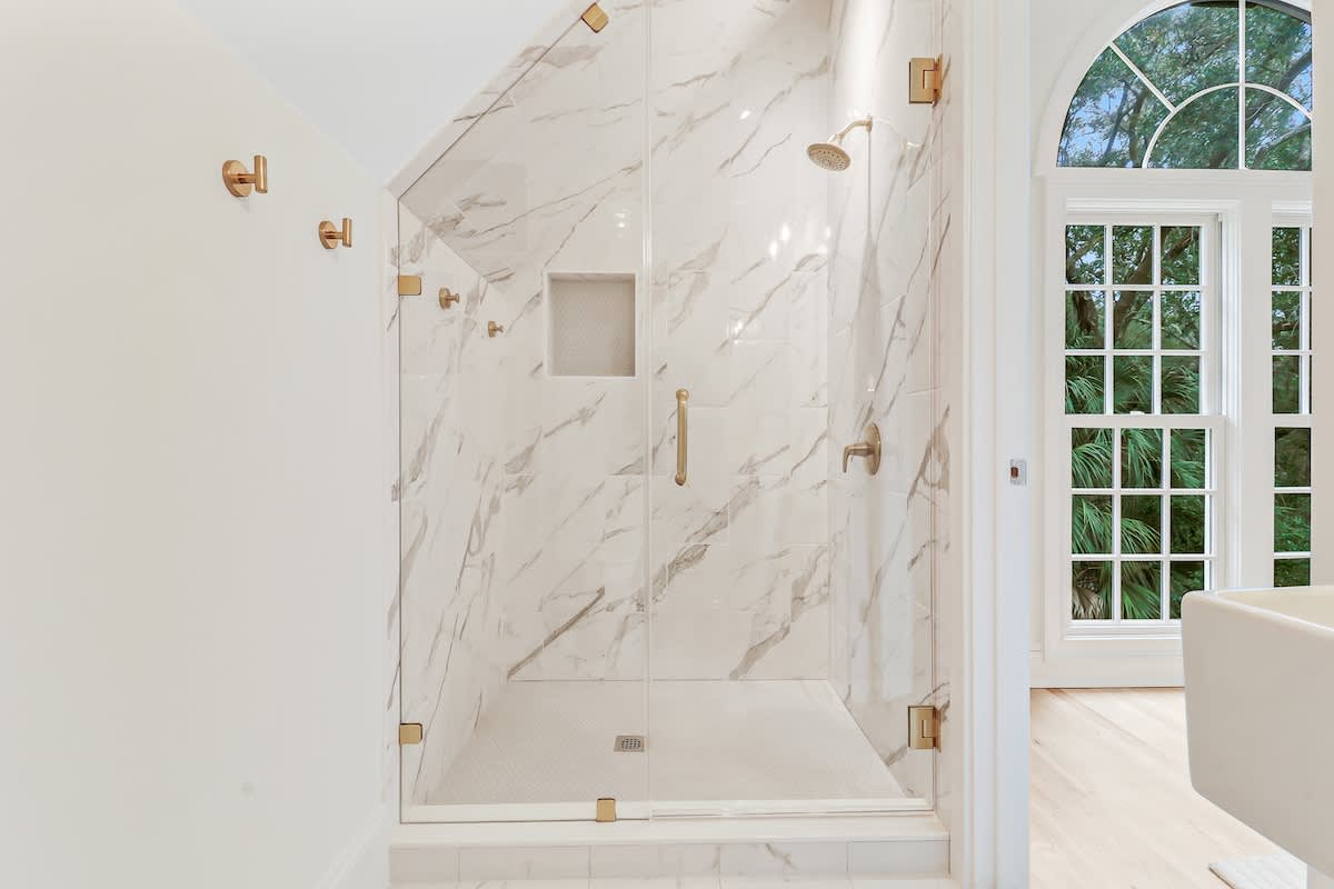 Step into your spa-like marble shower with elegant gold fixtures, where morning light streams through garden windows.