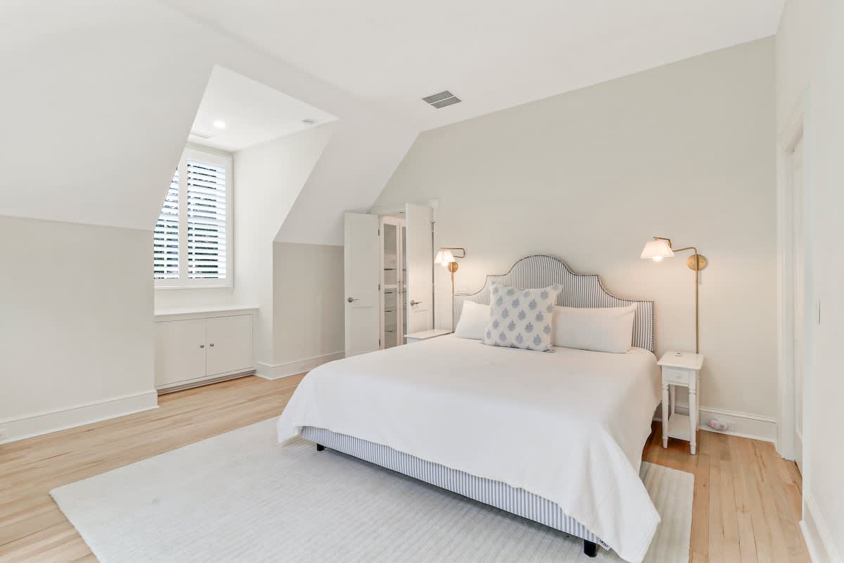 Relax in your bright attic bedroom with cozy lighting, elegant furnishings, and peaceful white linens for restful nights.