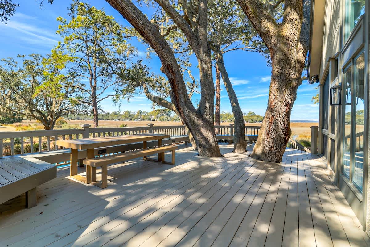Step onto your private deck where ancient oaks create natural shade above wooden benches, perfect for morning coffee with marsh views.