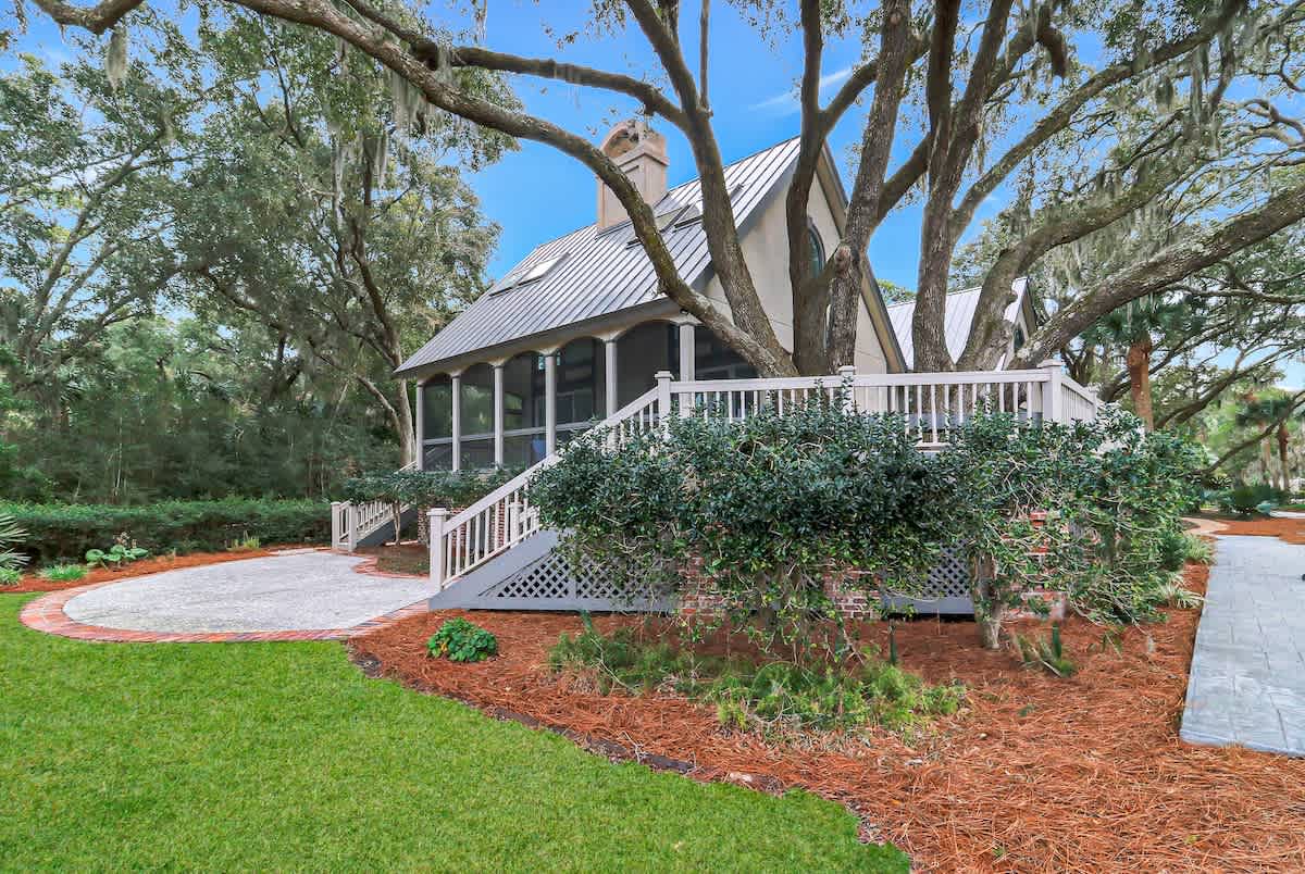 Charming property nestled among mature trees with wraparound porch and beautifully landscaped grounds featuring manicured lawn and garden beds.