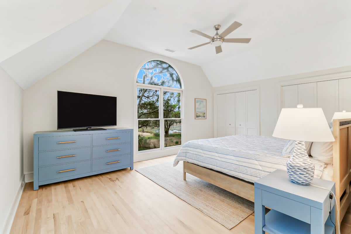 Unwind in this serene bedroom featuring soothing blue accents, vaulted ceilings, and peaceful garden views through arched windows.