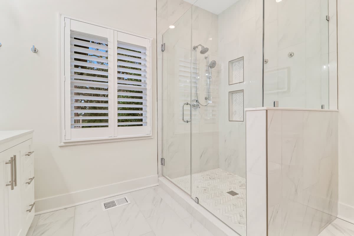 Step into your pristine marble bathroom featuring a luxurious glass-enclosed shower with dual fixtures for your ultimate comfort.