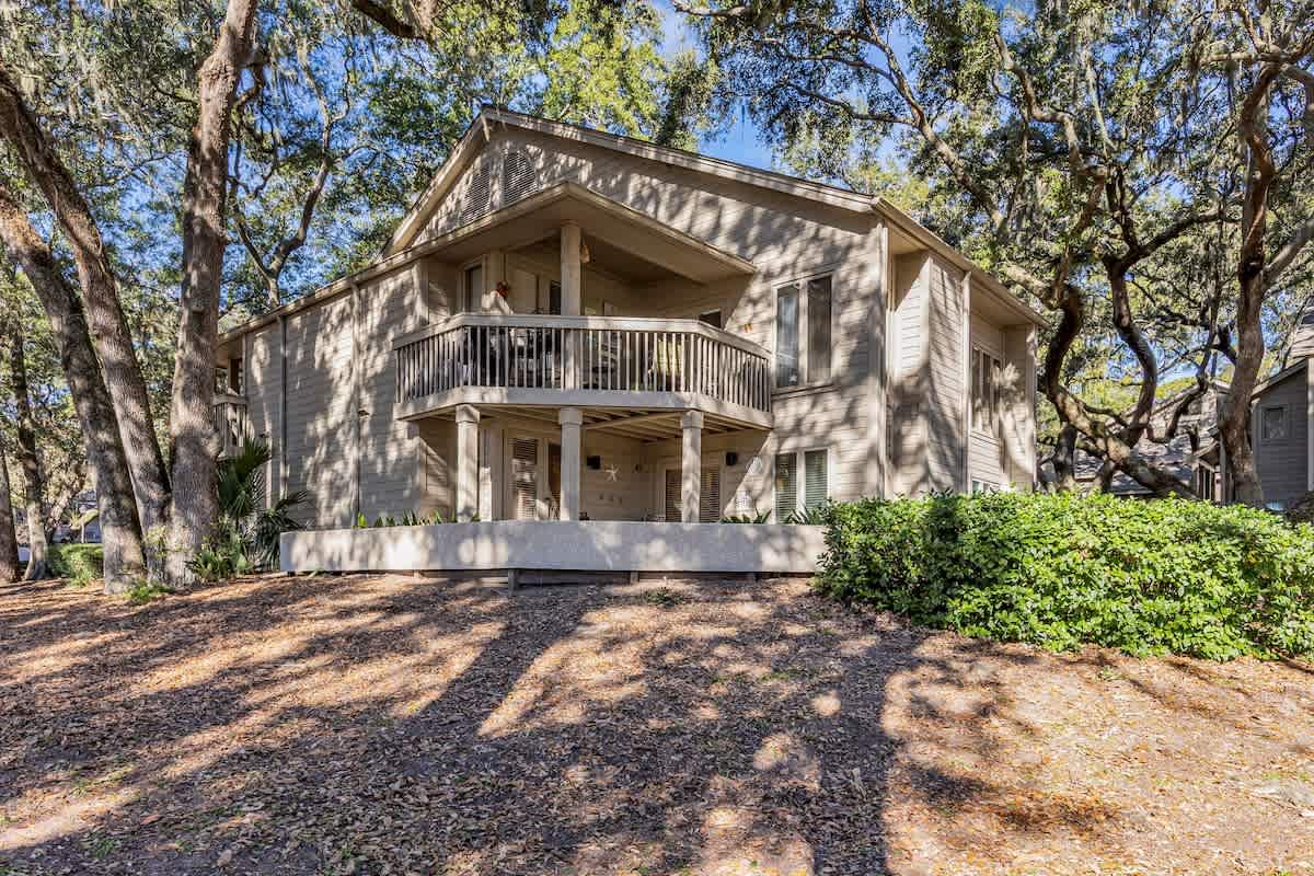 Two-story vacation home nestled among mature trees with covered balconies and natural landscaping in a peaceful wooded setting.