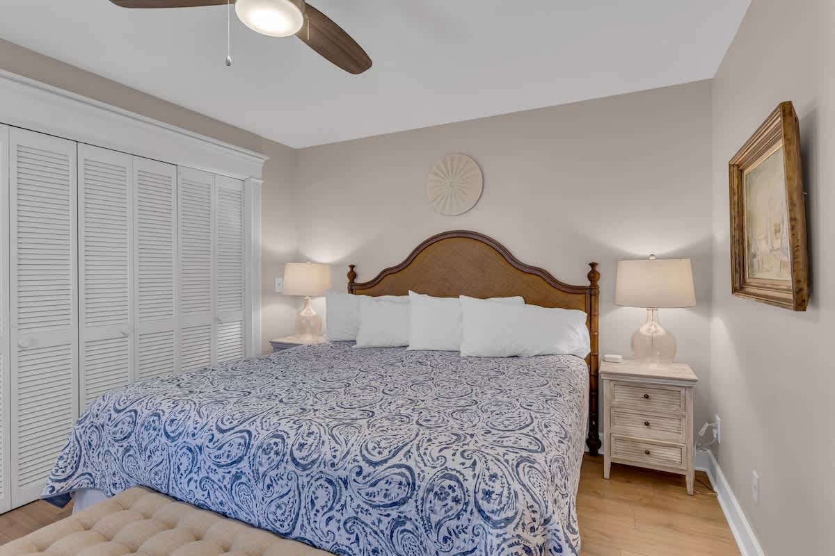Drift off to peaceful sleep in your elegant bedroom, featuring a plush king bed with coastal-inspired linens and gentle ceiling fan.