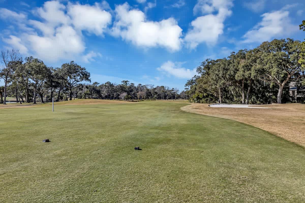 Pristine golf course with manicured greens surrounded by mature trees under a brilliant blue sky.