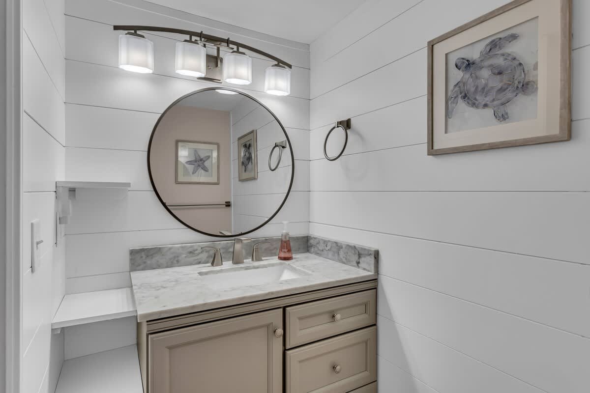 Refresh in your elegantly appointed bathroom featuring marble countertops, coastal artwork, and warm lighting that creates a serene spa-like atmosphere.