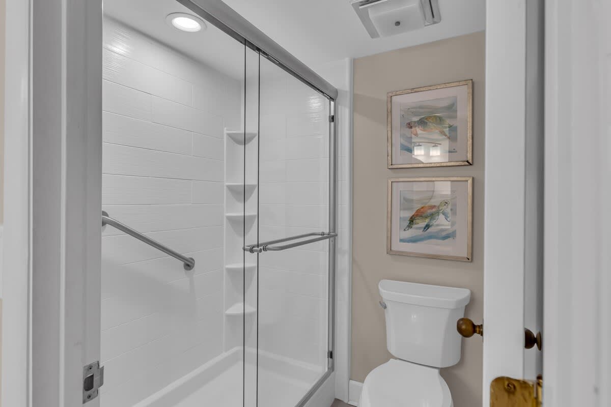 Step into your private sanctuary with a gleaming glass-enclosed shower and thoughtful coastal artwork that sets a serene, spa-like mood.