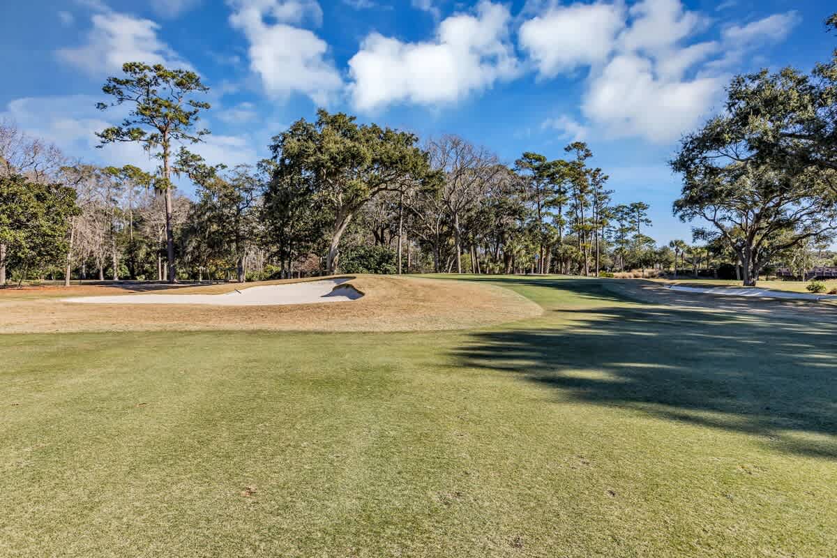 Championship golf course featuring manicured fairways and sand bunkers surrounded by mature oak trees under bright blue skies.