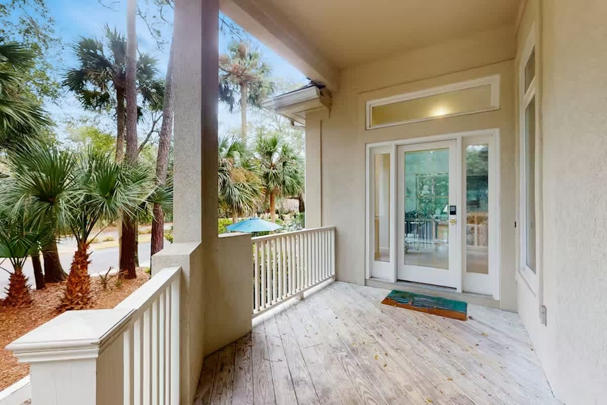 Step onto your private covered porch where tropical palms frame peaceful pool views through elegant railings.