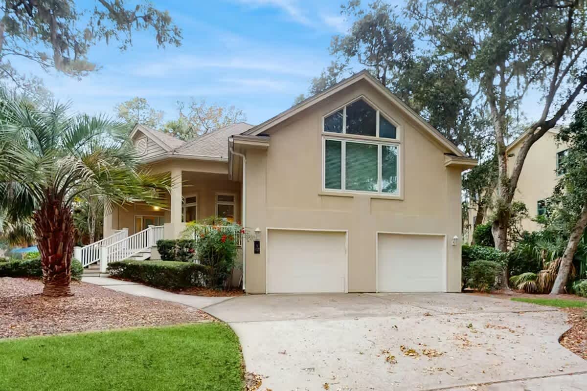 Charming two-story vacation home with tropical landscaping and two-car garage nestled among mature oak trees.