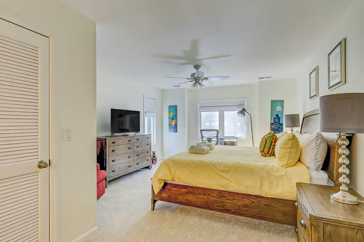 Relax in your bright, cheerful bedroom with golden linens and coastal touches. The ceiling fan keeps you cool while colorful artwork adds personality.