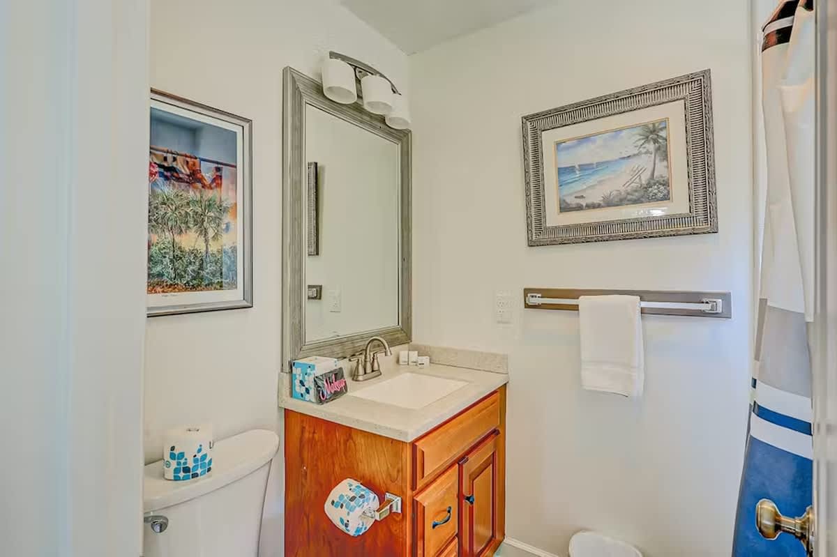 Your private bathroom features warm wood vanity, coastal artwork, and fresh towels—everything you need to refresh after beach adventures.