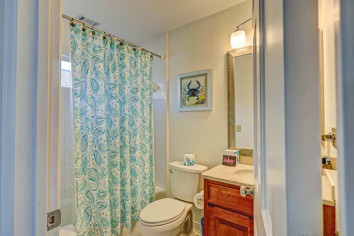 Refresh in your private bathroom with coastal charm—paisley curtain, warm wood vanity, and nautical artwork create a welcoming retreat.