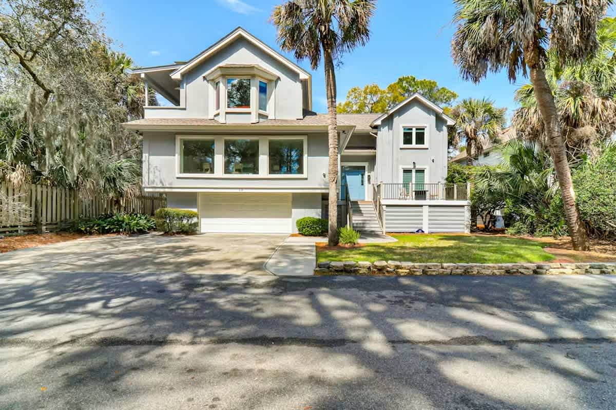 Modern coastal home nestled among towering palms and lush landscaping on a quiet residential street.
