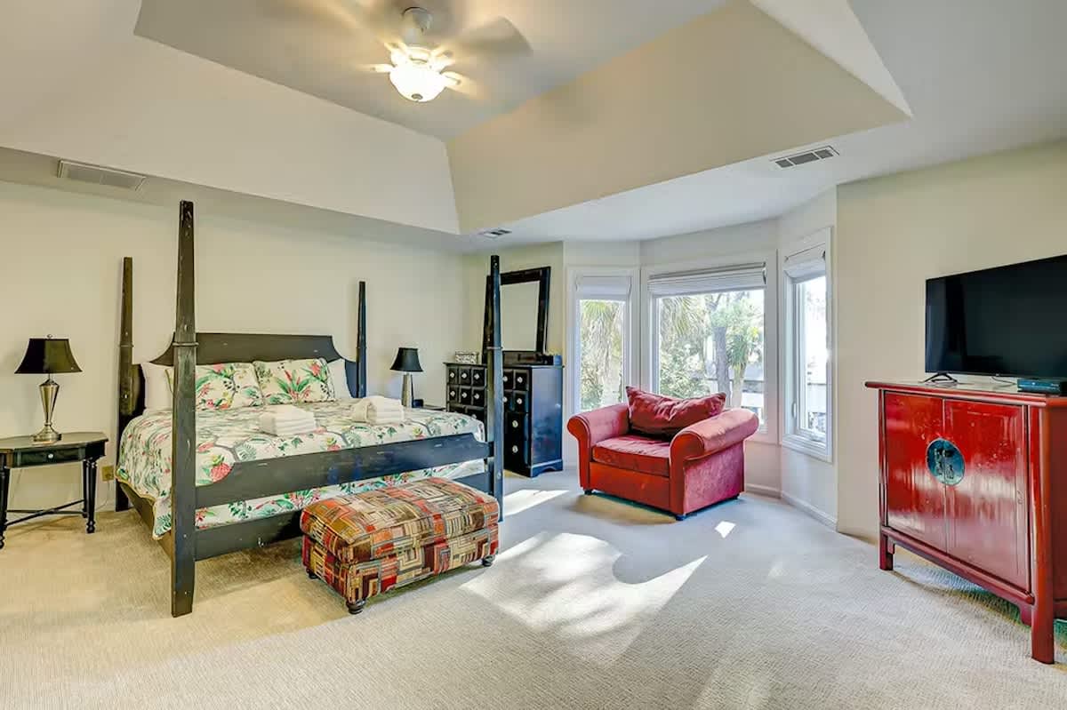 Unwind in your spacious master suite featuring elegant four-poster bed, cozy reading chair, and tropical garden views through expansive windows.