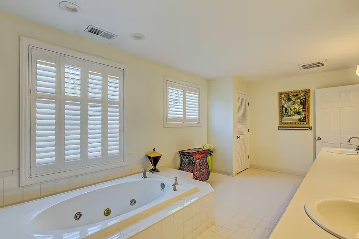 Soak in your private jetted tub beneath elegant plantation shutters, where warm afternoon light creates the perfect spa-like sanctuary for pure relaxation.