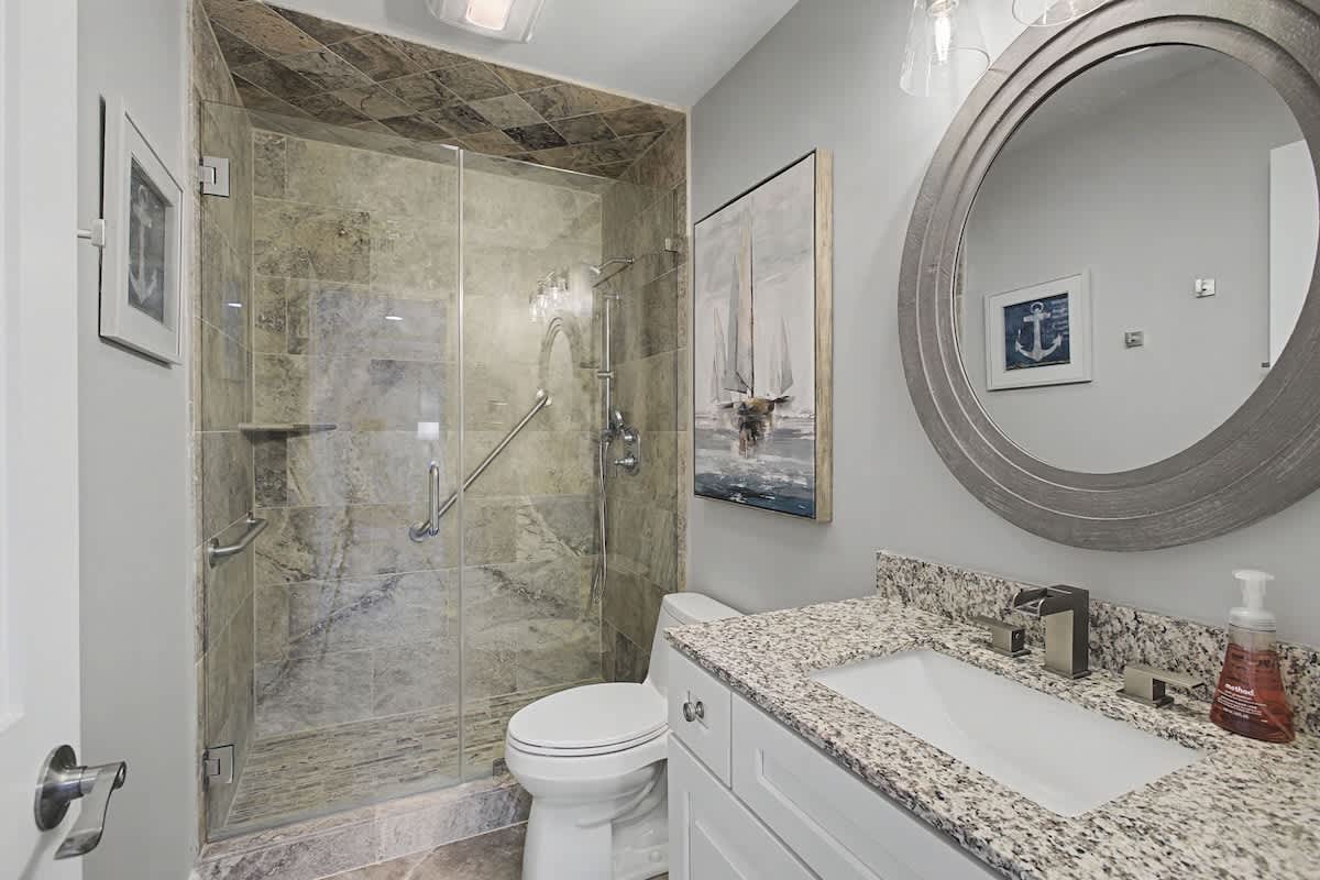 Step into your beautifully appointed bathroom featuring a luxurious stone-tiled shower, granite countertops, and elegant coastal decor that makes your daily routine feel like a spa retreat.