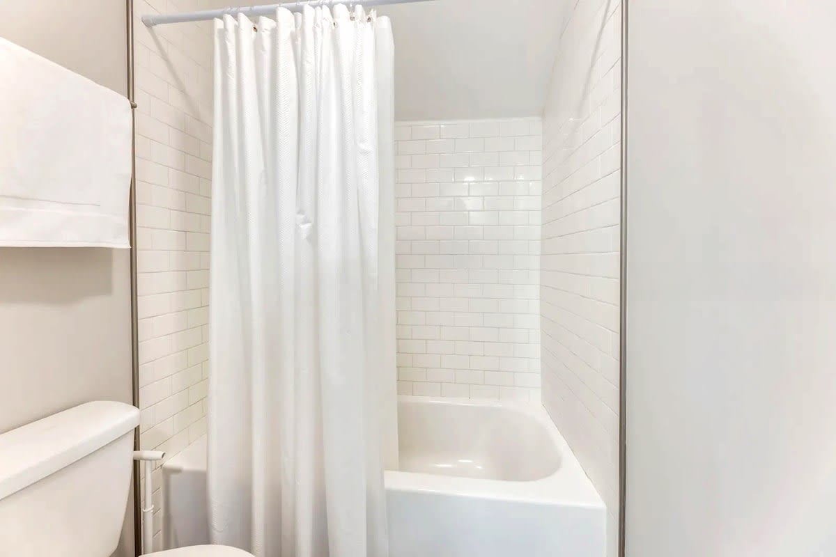 Refresh in your pristine bathroom featuring a gleaming tub-shower combo with classic subway tiles and crisp white curtains.