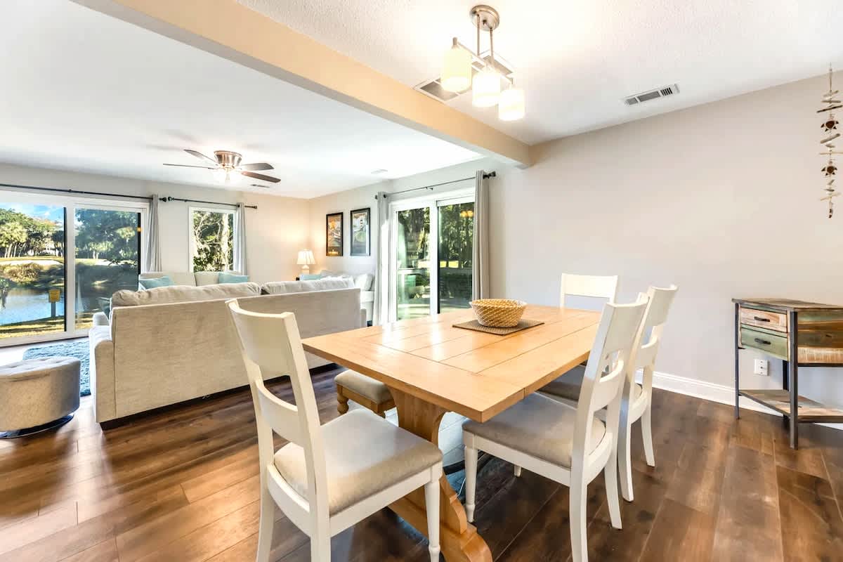 Your open-plan dining and living space features warm hardwood floors and large windows overlooking lush greenery, creating a bright and welcoming atmosphere for meals and relaxation.