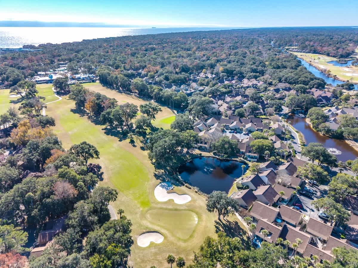 Aerial view of a coastal resort community featuring golf course fairways, waterways, and ocean access in a tree-lined setting.