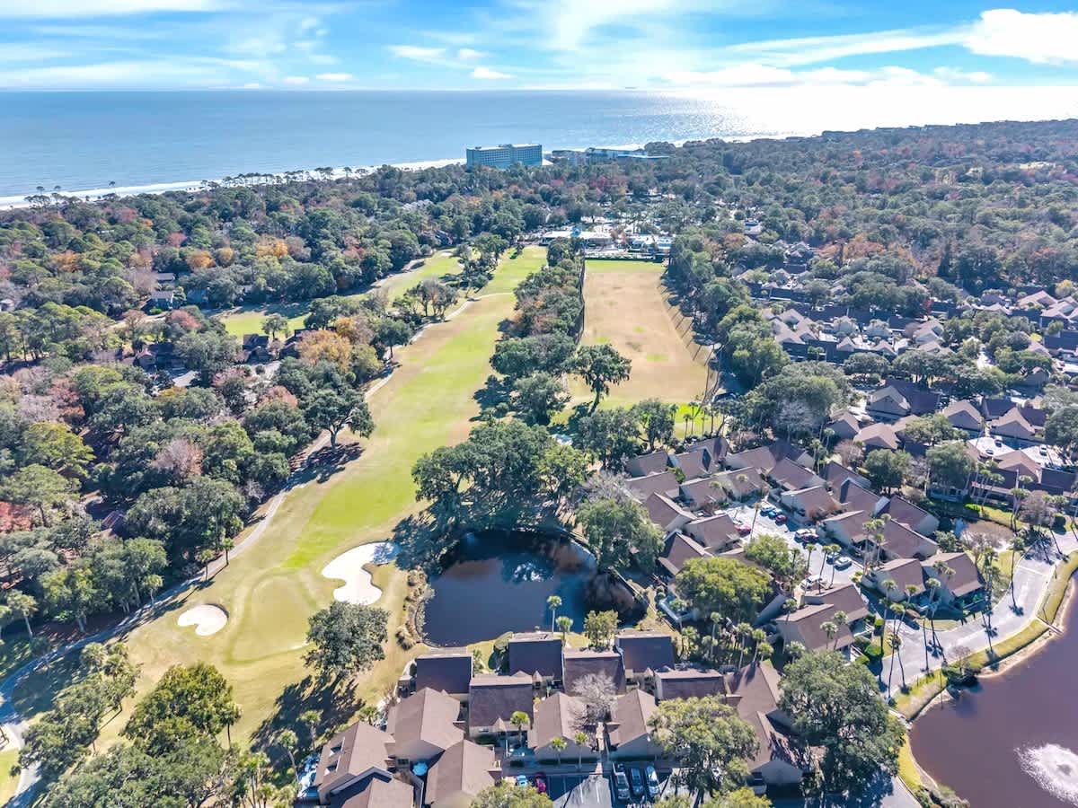 Aerial view of a stunning coastal community featuring golf course fairways, waterfront homes, and pristine beachfront access.