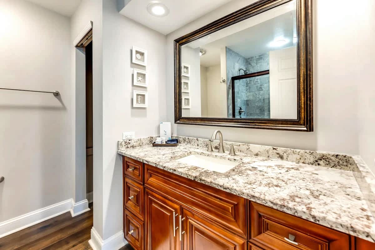 Refresh in your elegant bathroom featuring granite countertops, rich wood cabinetry, and a pristine marble-tiled shower behind you.